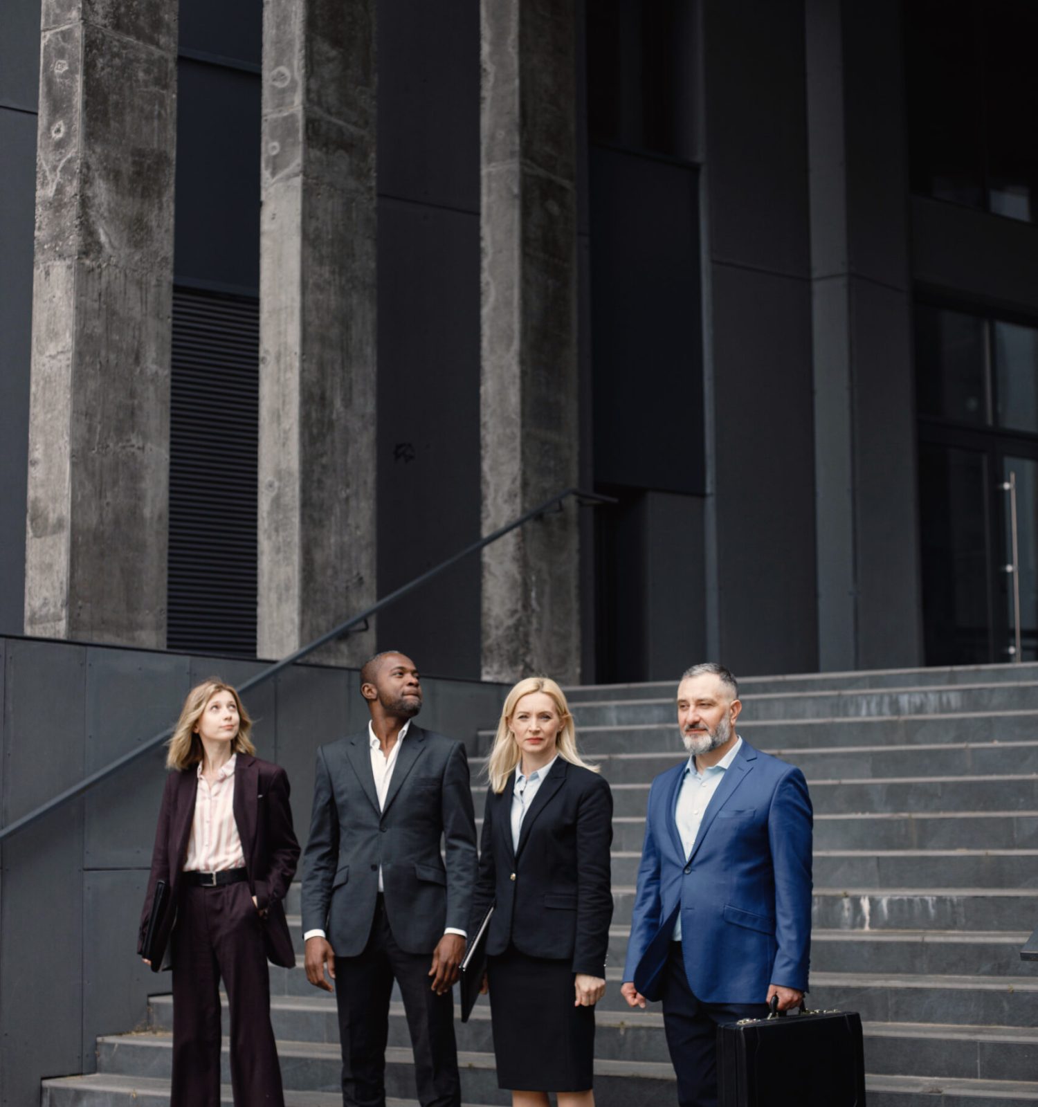 Confident businesspersons standing in front of modern office building. Men and women talking and holding documents. Banking and financial market concept.