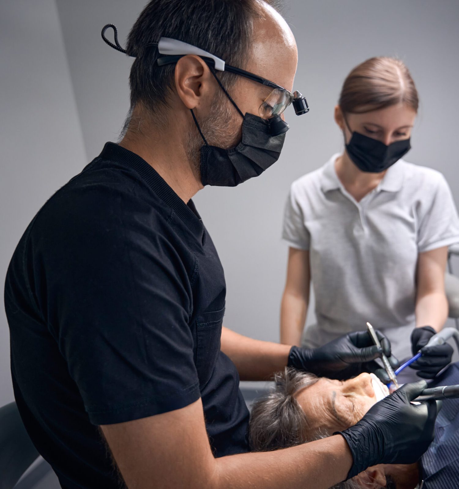 Dentist prosthetist with assistant restore teeth of woman, man uses binocular dental glasses