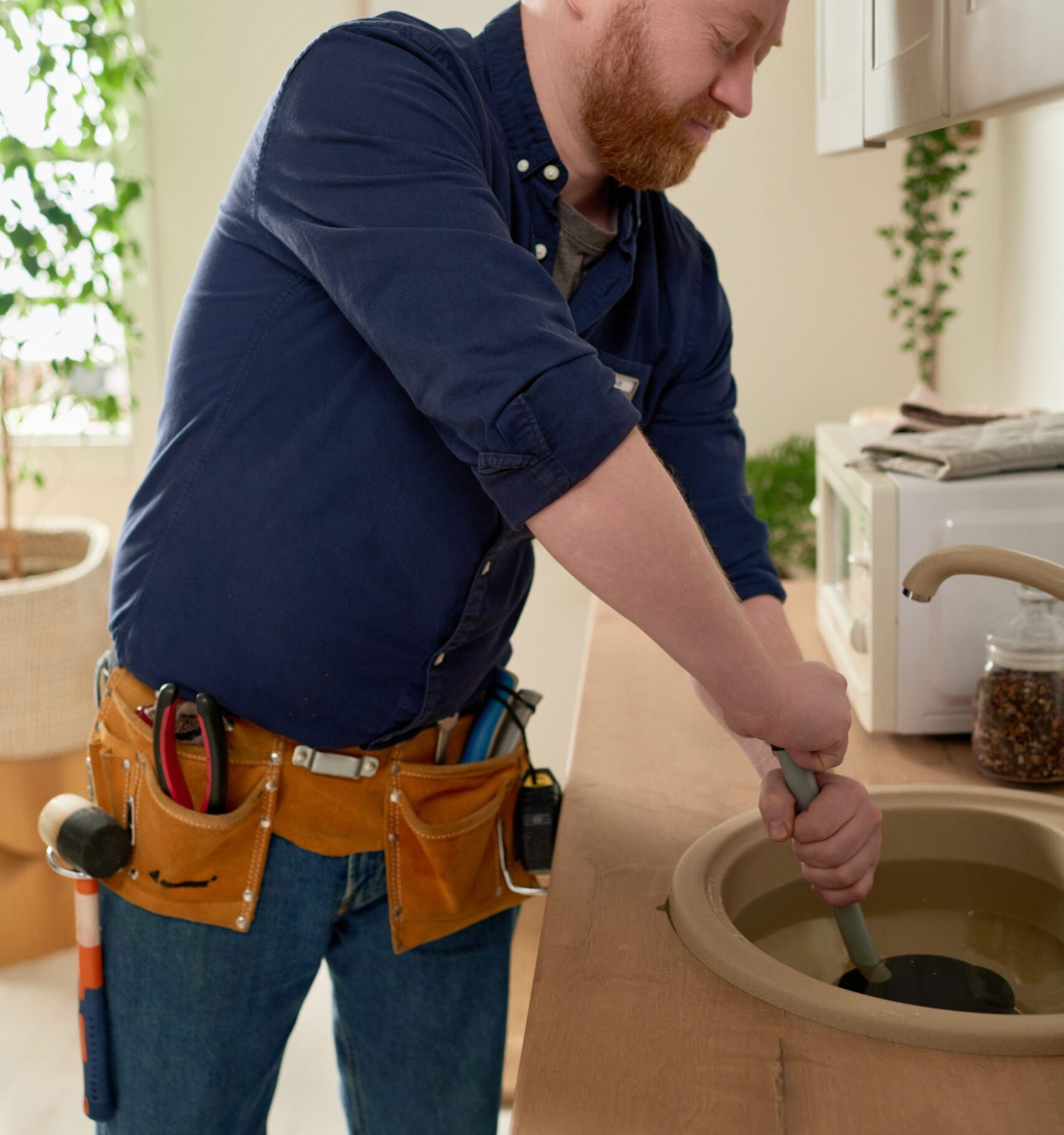 Mature worker repairing blockage in the sink with special equipment during his work in domestic kitchen